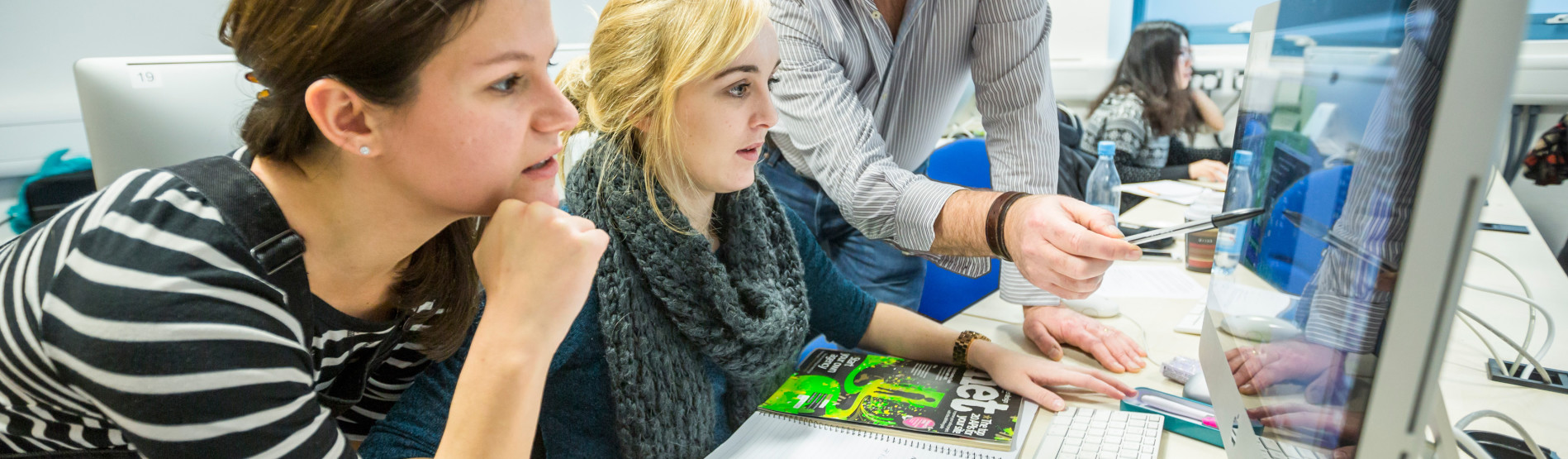 Students at a computer in a CAD lab being instructed by a lecturer