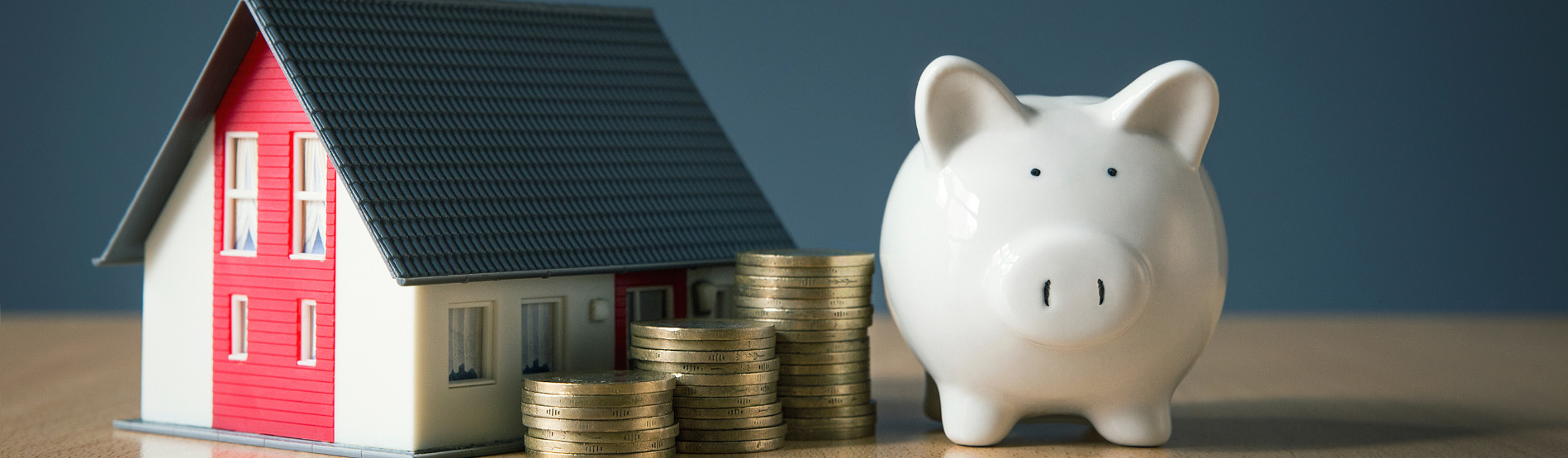 Piggy bank, toy house and coins in a row 