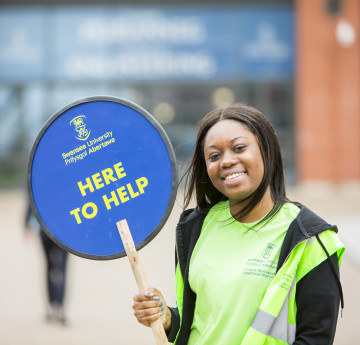 Student ambassador similing with a 'Here to help' sign 