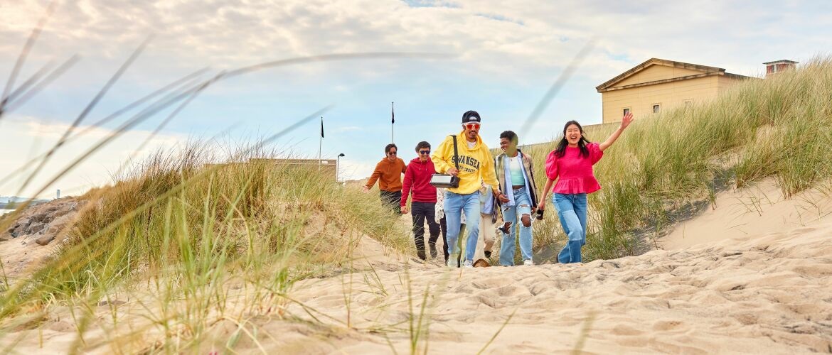 picture of students walking on the beach by Bay Campus with the Great Hall in the background