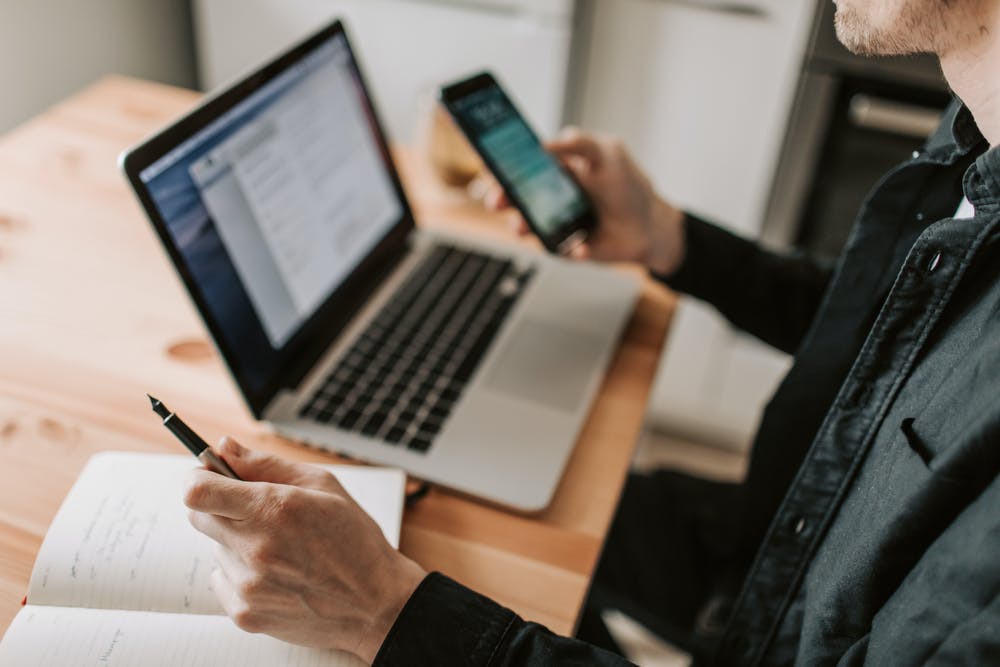 image of a person holding a phone and working on a laptop