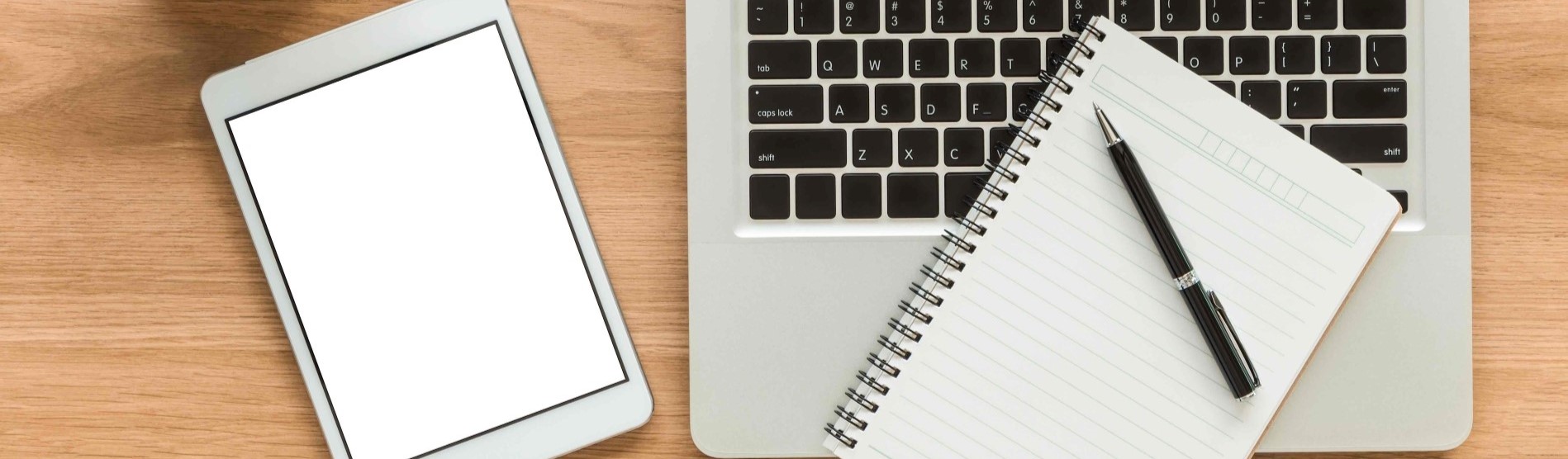 Stock image of tablet, laptop PC and notebook and pen on a desk.