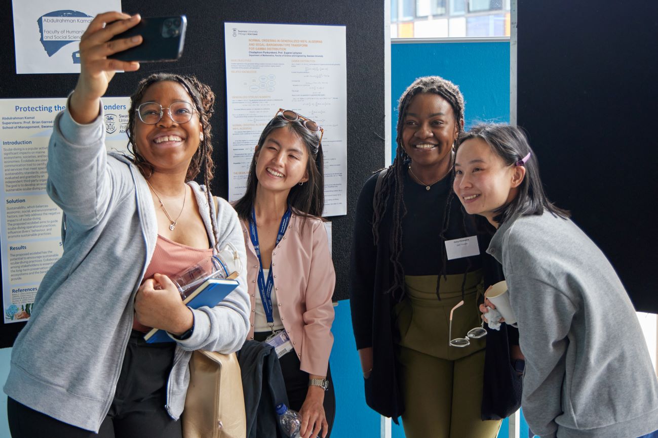 A group of four people taking a selfie in front of research posters