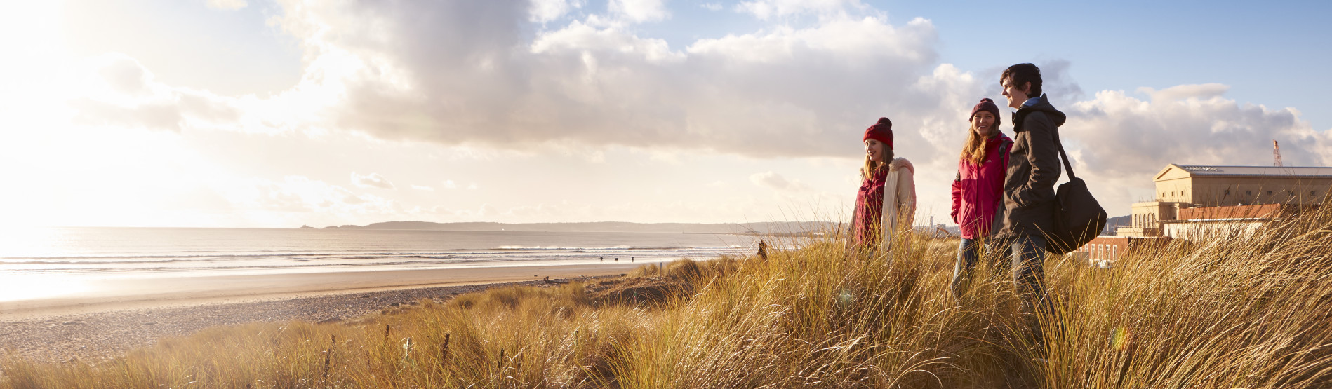 Three students standing on the dunes at bay campus looking out to sea