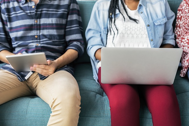 Two students sitting side by side, one on a laptop and the other on a tablet