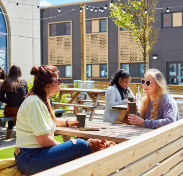 Two students sitting outside Tafarn Tawe, a Students' Union bar. It's sunny and they are wearing sunglasses.