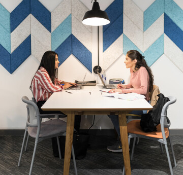 Two females, working on laptops in a study space.